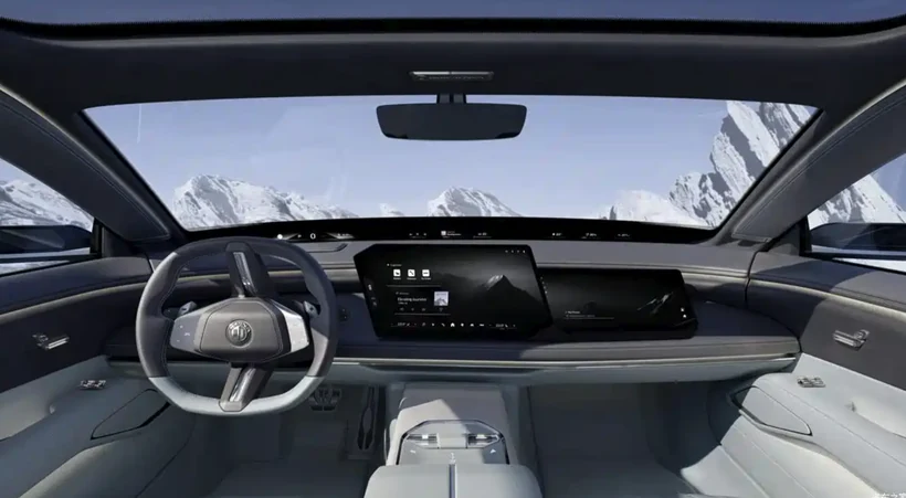 图片展示了展示了BMW Vision Alpina Concept概念车的内饰。车内以浅灰色为主，中控台配备大尺寸的触摸屏，屏幕下方有空调出风口。方向盘为三幅式设计，带有BMW标志。车门处有银色把手，车顶为全景天窗。车窗外是雪山景观，天空呈淡蓝色。此图与上文提到的车机主题色及车内细节相呼应